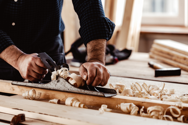 Carpenter's hands planing a plank of wood with a hand plane